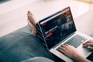An image featuring a person laying and watching Netflix on their laptop
