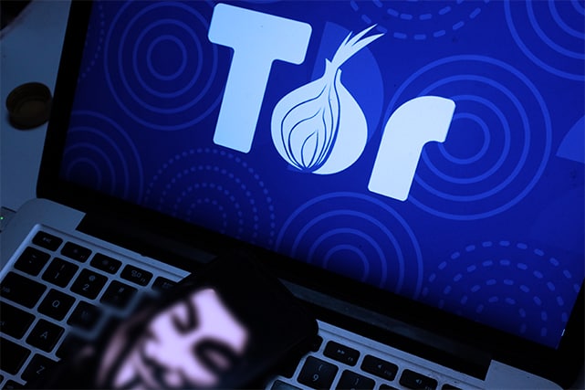 An image featuring a laptop with the Tor browser opened and an anonymous mask on the keyboard