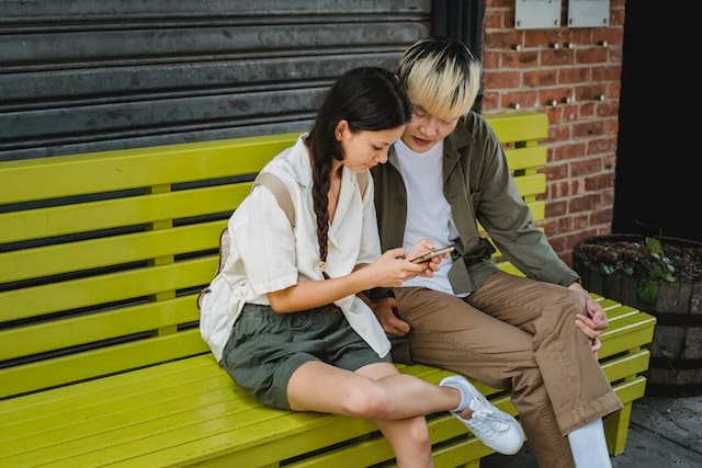 Young Asian couple using smartphone on street bench