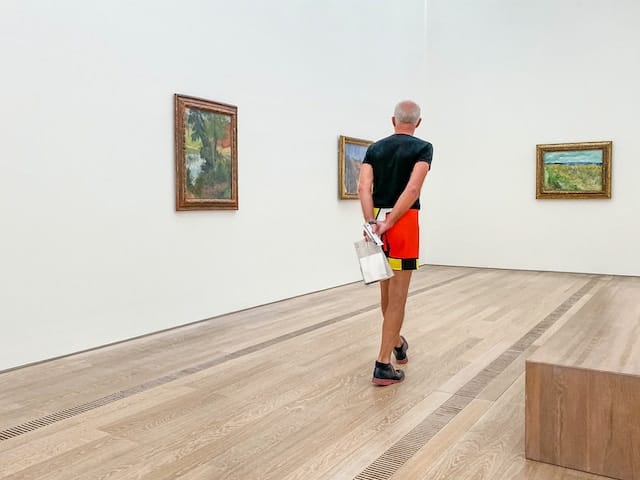 man standing in an art gallery looking at paintings